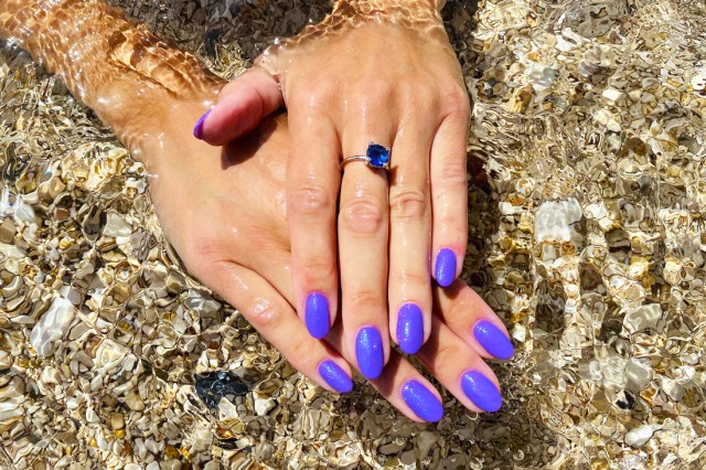 Close up of hands in water, long nails painted purple, wearing a blue ring