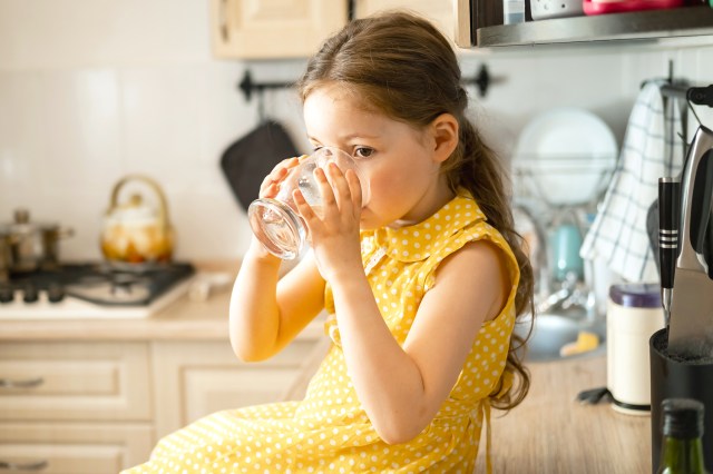 Little girl drinking water from a glass in the kitchen