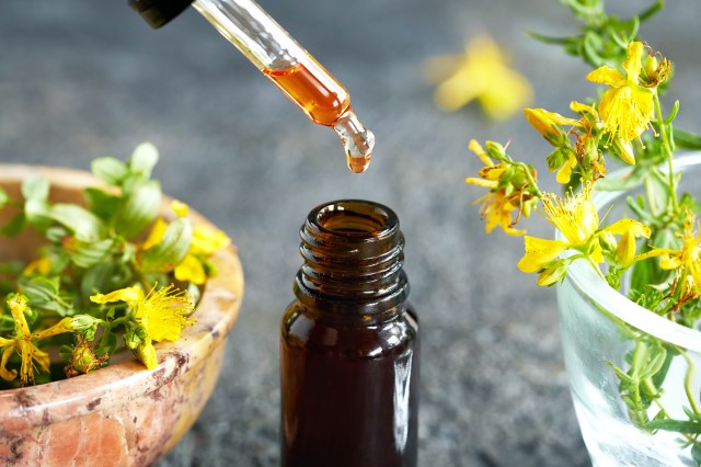 St. John's wort oil dropper and bottle next to fresh flowers