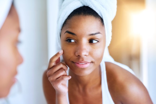 Close up of a woman looking at her face in the mirror, touching her cheek, towel on her head