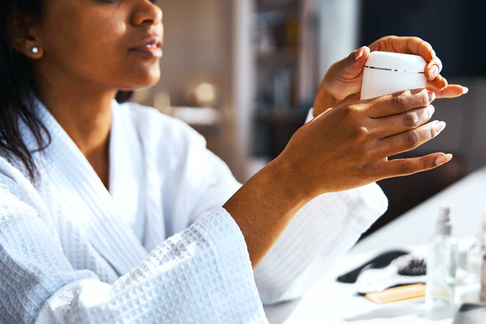 Woman in bathrobe holding skincare cosmetic product