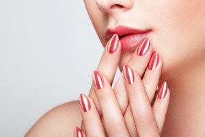Close up of shiny, painted nails touching woman's lips