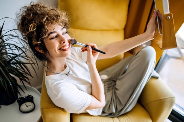 Young woman sitting in her living room putting on make-up