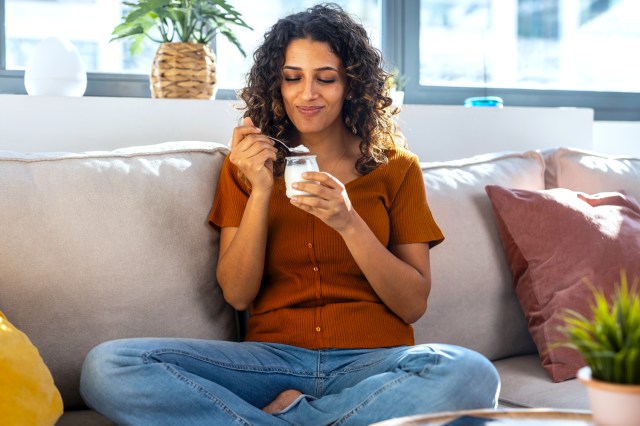 Smiling woman eating yogurt on sofa at home