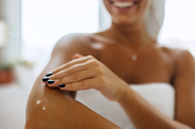 Close up of woman applying lotion to her arm, in a towel