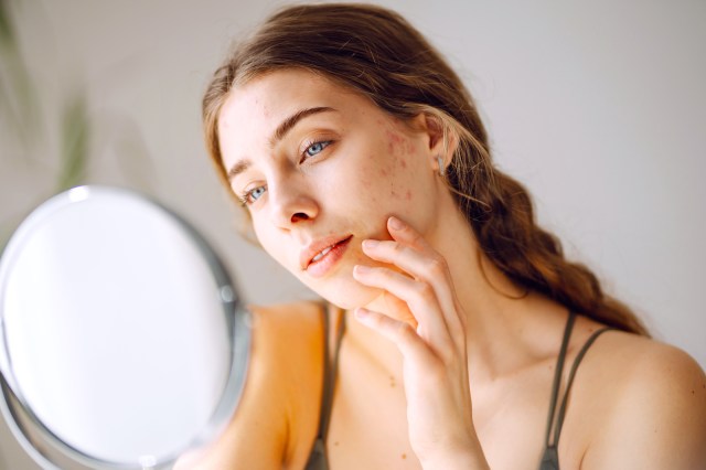 Woman looking at her skin in a mirror, blemishes