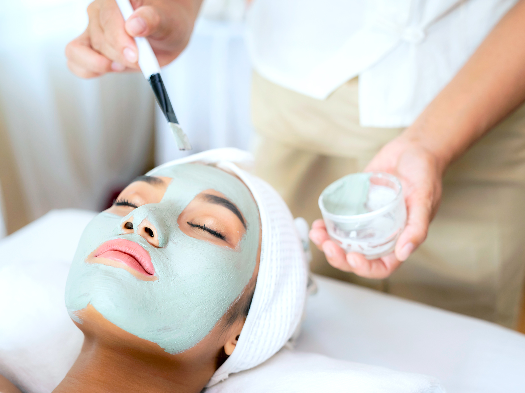 Woman getting facial clay mask at beauty spa