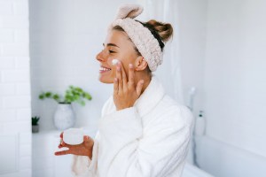 Woman applying face moisturizer in bathroom