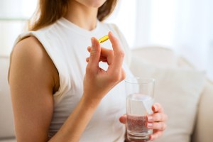 Woman holding supplement pill and glass of water