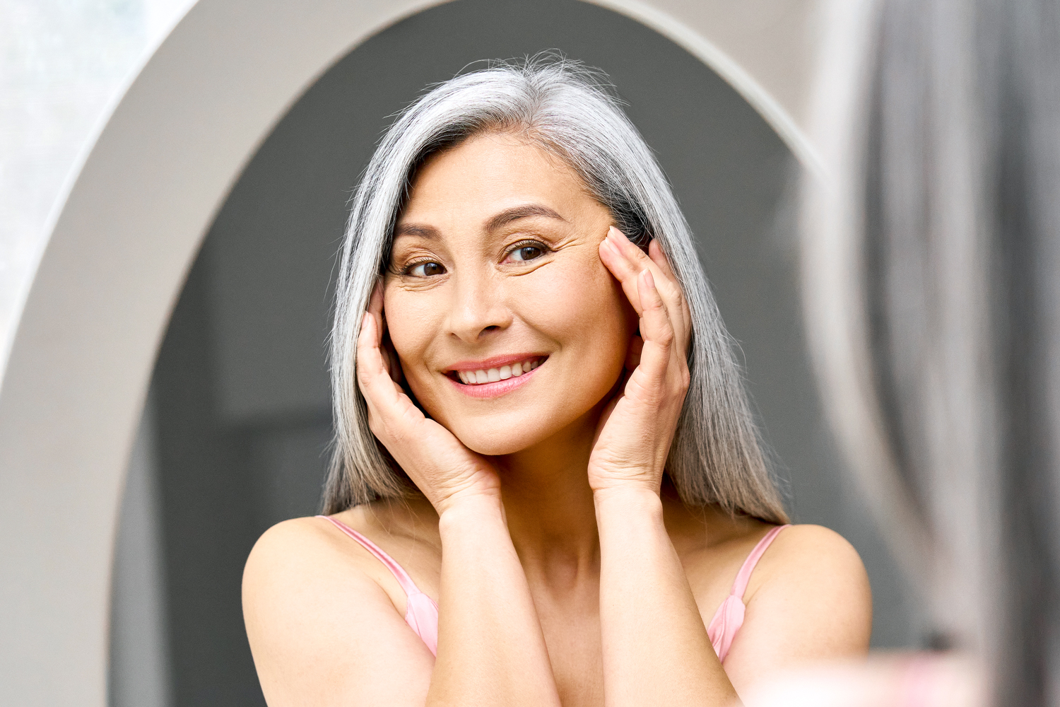 Happy mid aged Asian woman looking at mirror